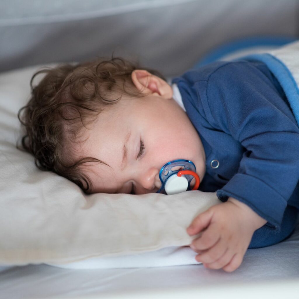 Baby sleeping peacefully with a pacifier, in a guide by a baby dentist in Dubai