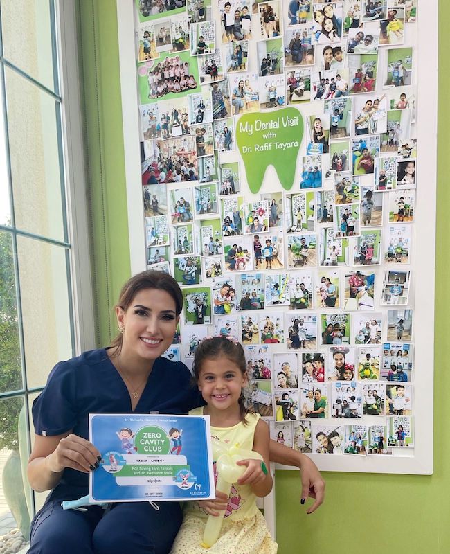 Dr. Rafif Tayara with a young patient in front of the ‘My Dental Visit’ photo wall at her clinic in Dubai