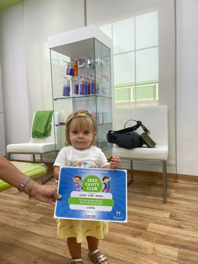 Toddler holding a Zero Cavity Club certificate after her first dental visit with a pediatric dentist in Dubai